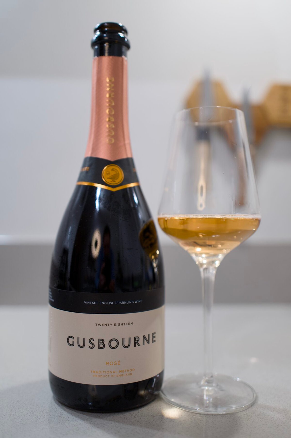 Gusbourne Rosé bottle with copper foil beside a glass of salmon-pink sparkling wine