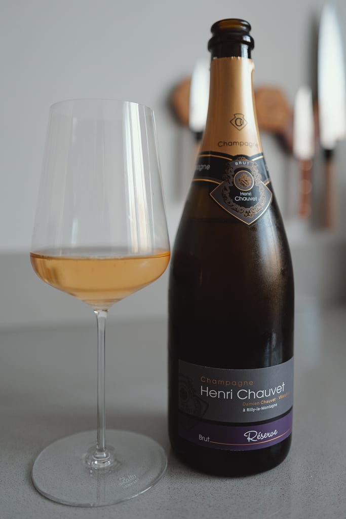 Henri Chauvet Réserve Champagne bottle with purple label beside a glass of golden wine
