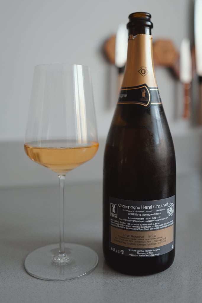 Henri Chauvet Champagne bottle shown back-label first beside a glass of golden wine