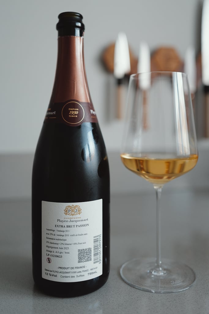 Back label of a Ployez-Jacquemart Extra Brut Passion Champagne bottle beside a glass