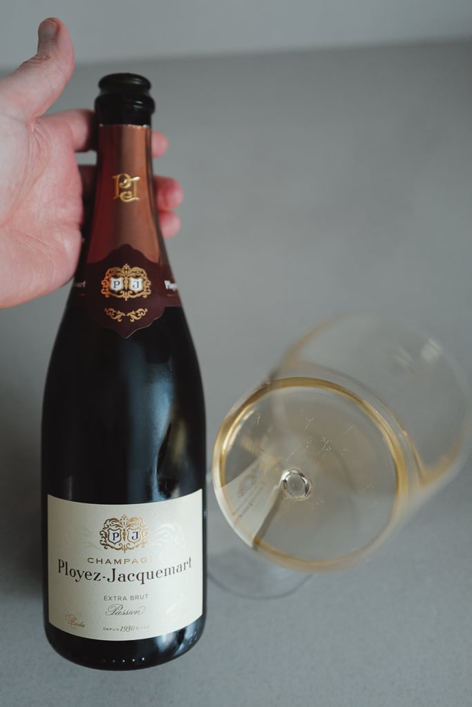 Hand holding a Ployez-Jacquemart Extra Brut Champagne bottle beside a glass of golden wine