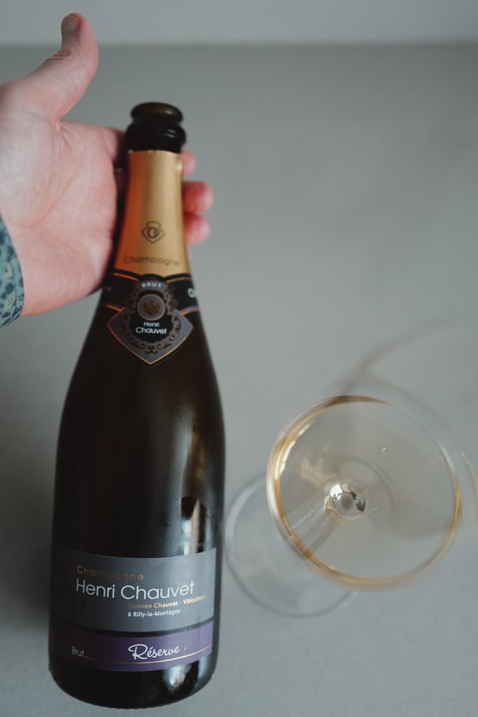 Hand holding a Henri Chauvet Réserve Champagne bottle next to a glass of golden wine