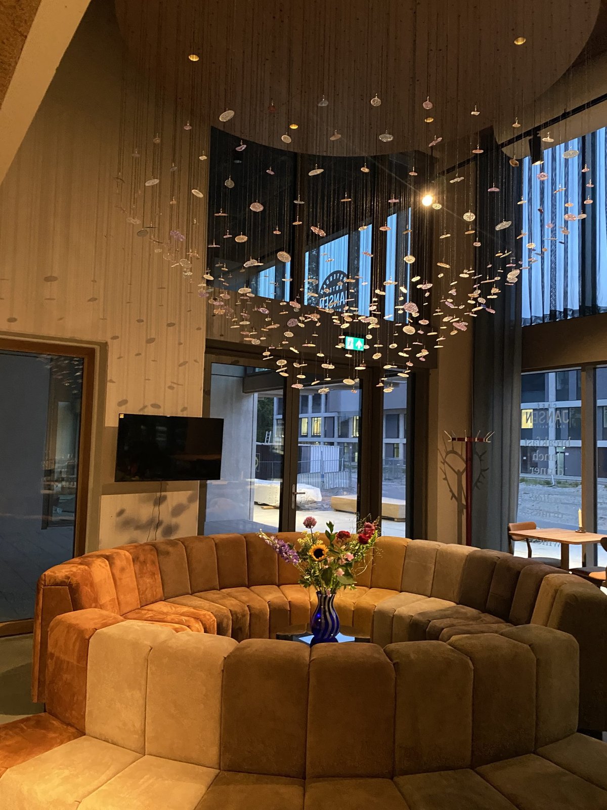 Double-height lobby with a curved tan sofa, flowers and a hanging light installation