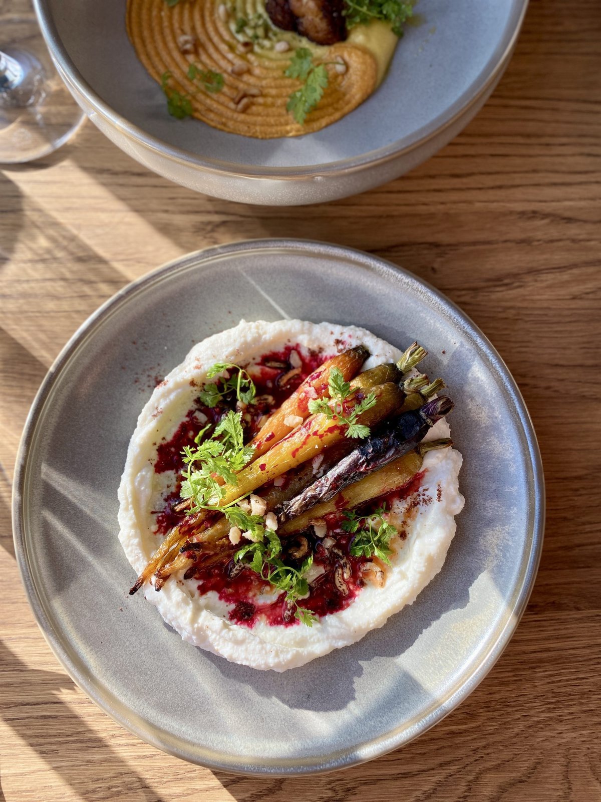 Roasted heritage carrots on whipped ricotta with beet sauce, nuts and herbs in a grey bowl
