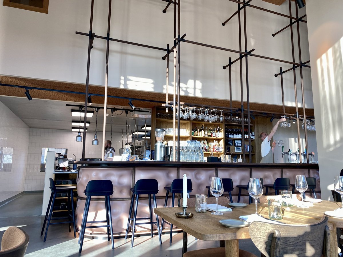 Wide view of the Cafe Jansen copper bar and dining tables under tall metal frames in daylight