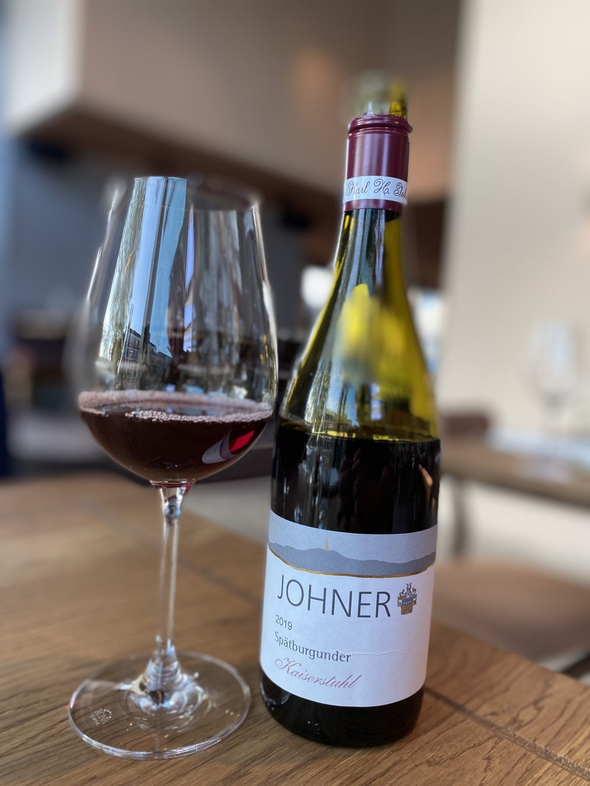 Glass of red wine beside a bottle of Johner 2019 Spatburgunder Kaiserstuhl on a wooden table