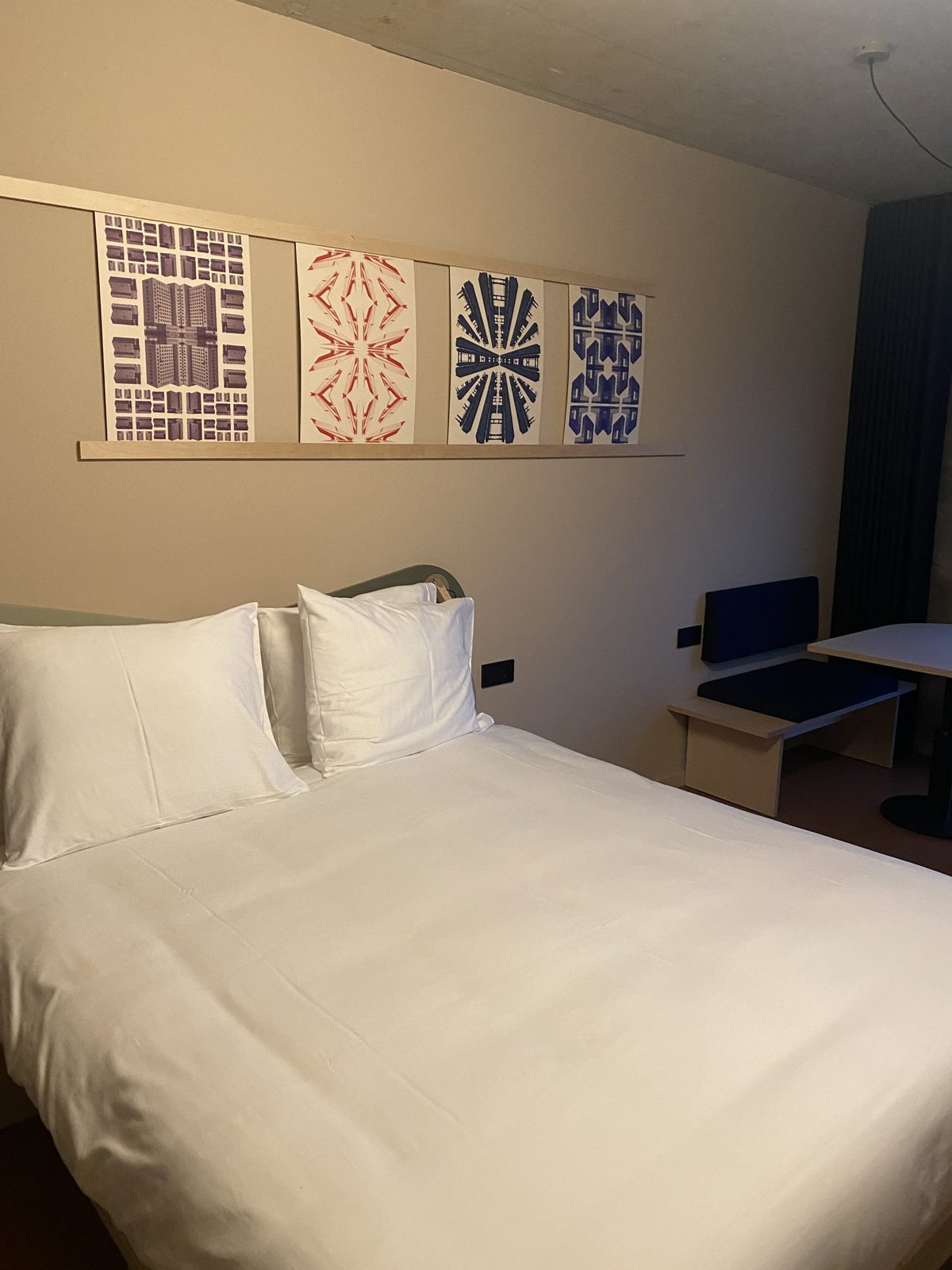 Hotel bedroom with a white double bed and four framed graphic prints of the old prison towers
