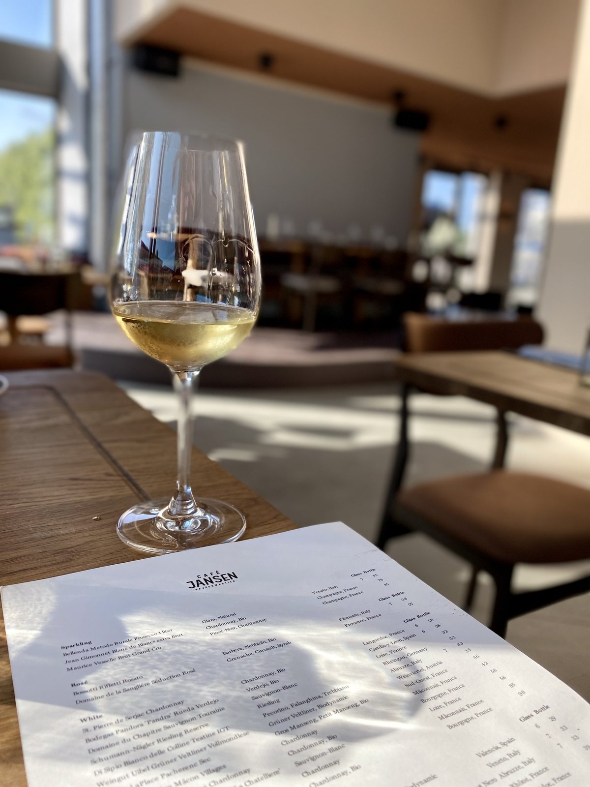 Glass of white wine on a table with the Cafe Jansen wine list, bright dining room behind