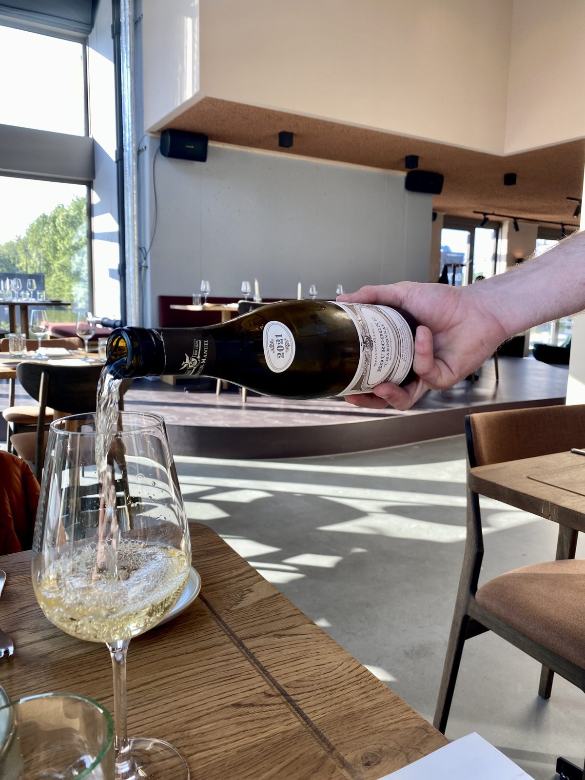 Sparkling wine being poured into a glass at a sunlit table in the Cafe Jansen dining room