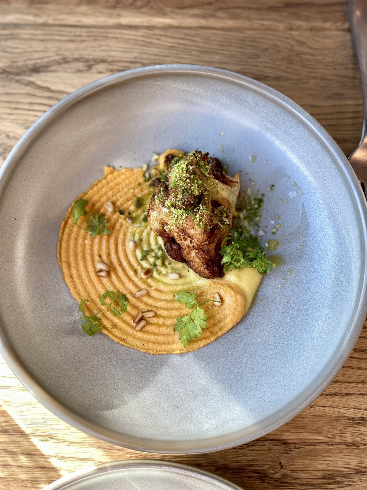 Plated dish of roasted meat on swirled puree with herbs and pine nuts in a grey bowl