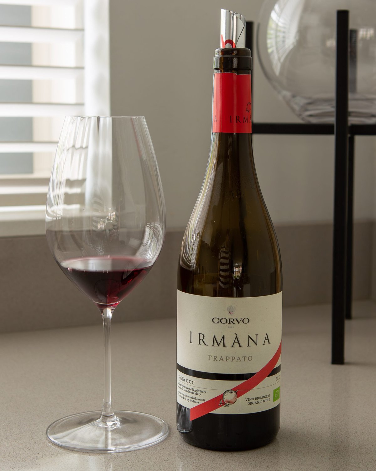 Bottle of Corvo Irmana Frappato organic Sicilian red beside a glass of pale red wine