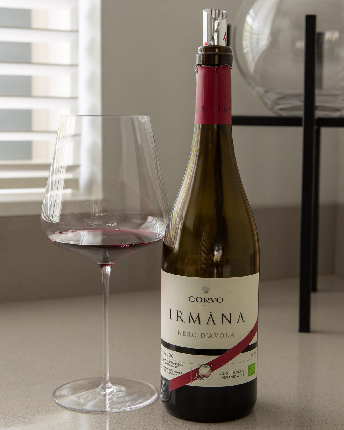 Bottle of Corvo Irmana Nero d'Avola organic Sicilian red beside a glass of red wine