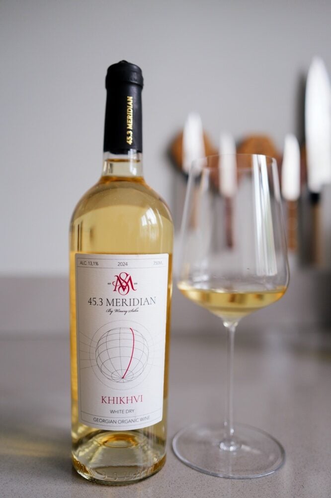Bottle of 45.3 Meridian Khikhvi 2024 Georgian white wine next to a glass of pale white wine