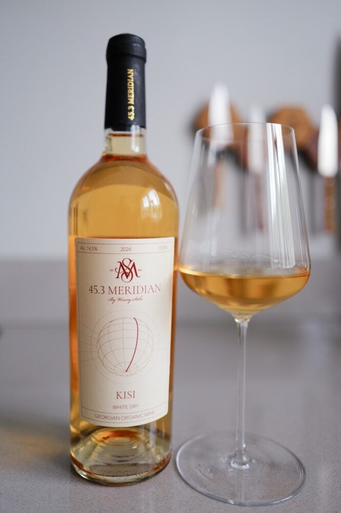Bottle of 45.3 Meridian Kisi 2024 Georgian white wine beside a glass of golden white wine