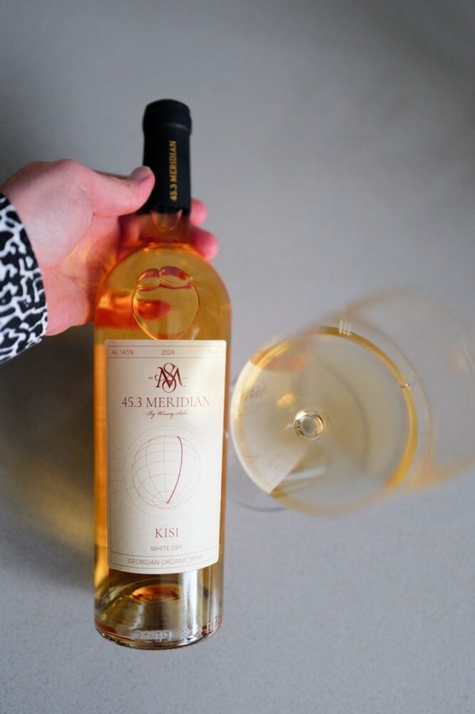 Hand holding the 45.3 Meridian Kisi 2024 bottle above a glass of deep golden white wine