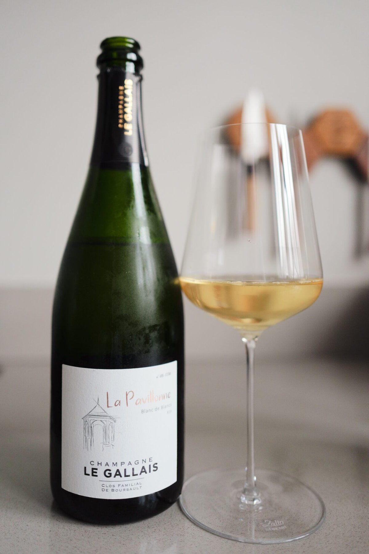 Green bottle of Champagne Le Gallais La Pavillonne next to a glass of golden champagne