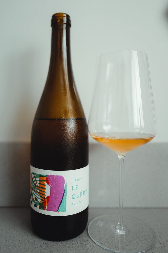 Brown bottle of Pierre Goiset Le Query Muscadet beside a glass of amber-orange wine