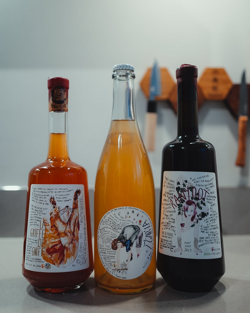 Three Les Jardins En-Chantants natural wine bottles lined up against a kitchen wall