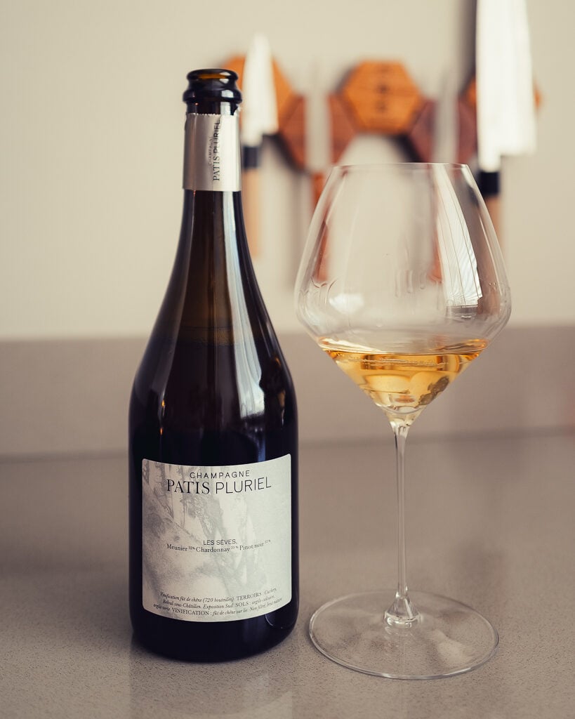Patis Pluriel Les Seves bottle beside a glass of deep golden champagne