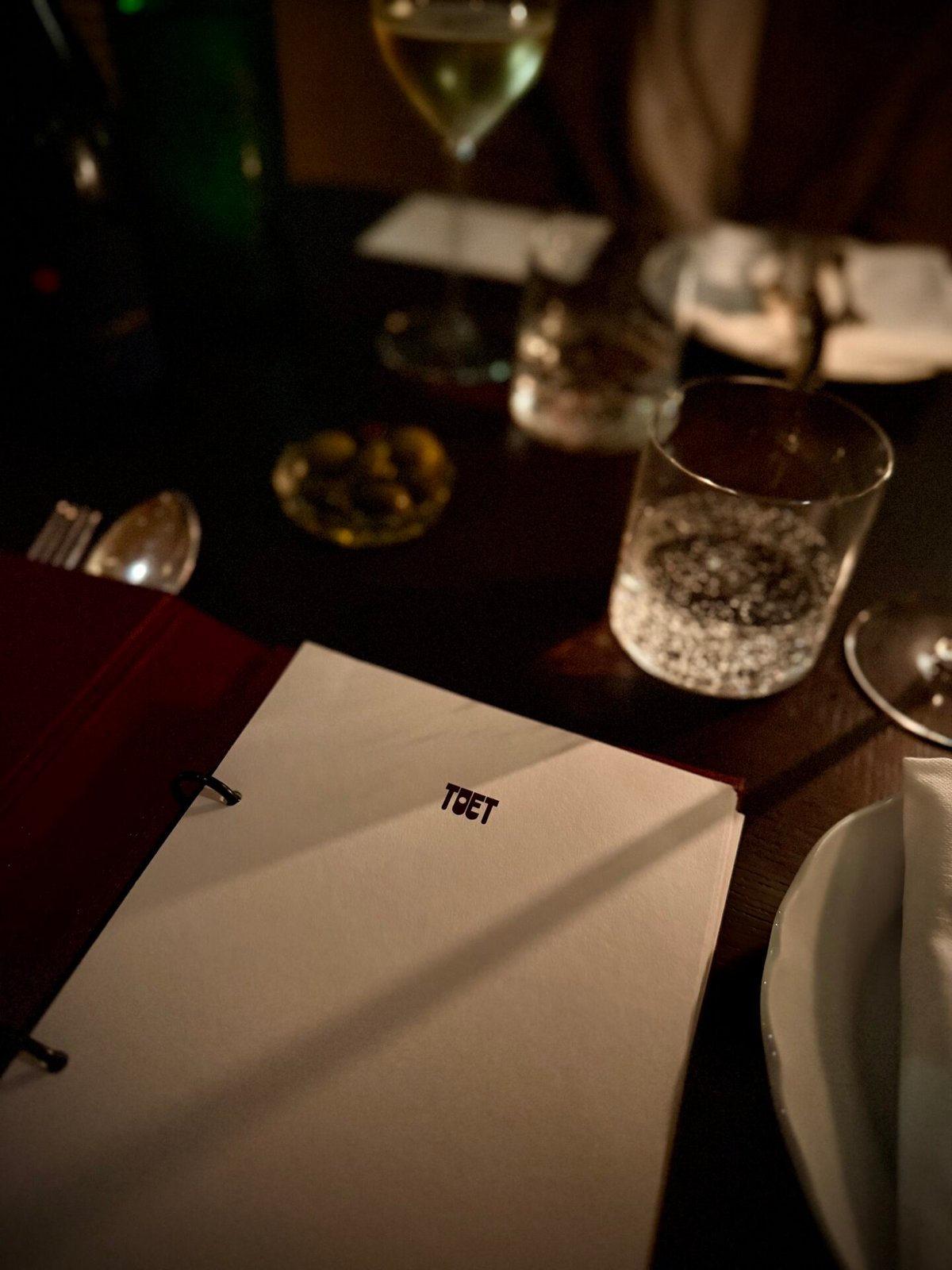 Toet menu folder on a dark wooden restaurant table beside a water glass in low light