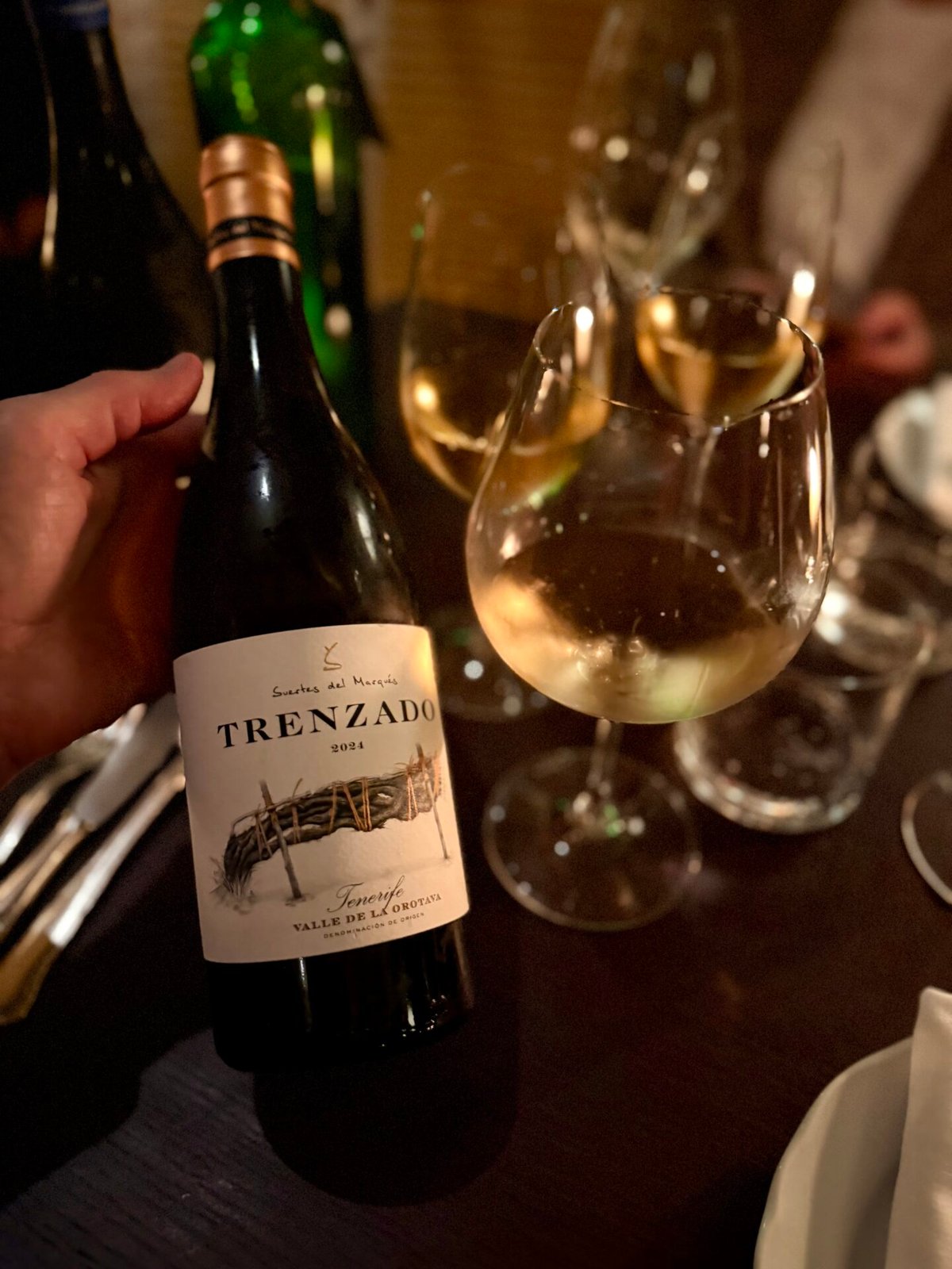 Man seated at a restaurant table checking his phone with three glasses of white wine in front
