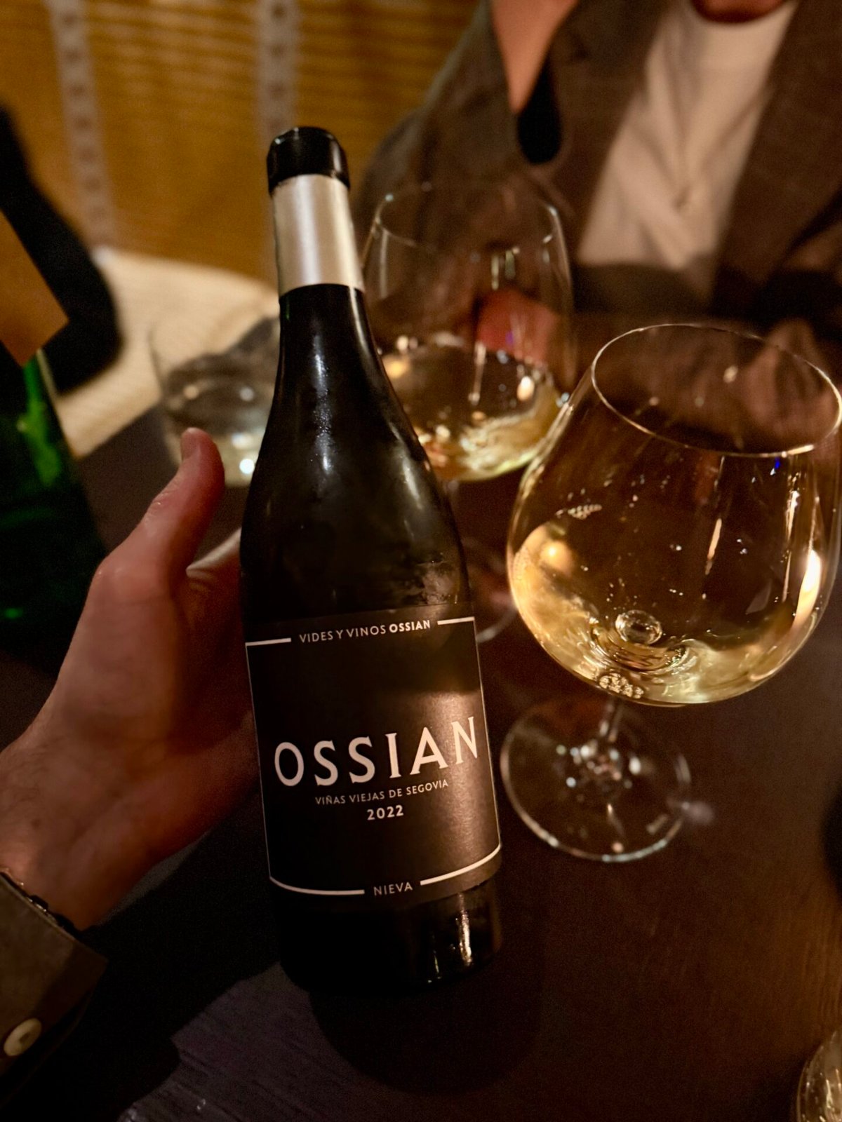 Hand holding an Ossian Viñas Viejas Verdejo bottle beside glasses at a restaurant table