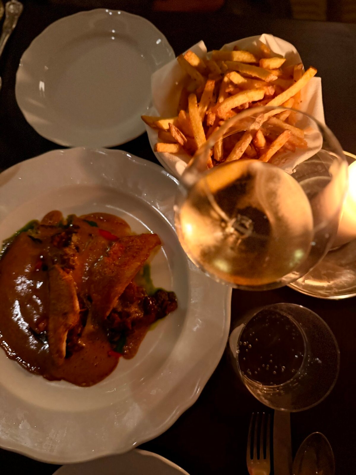 Main course of fish in sauce with a basket of fries and white wine on a dark table