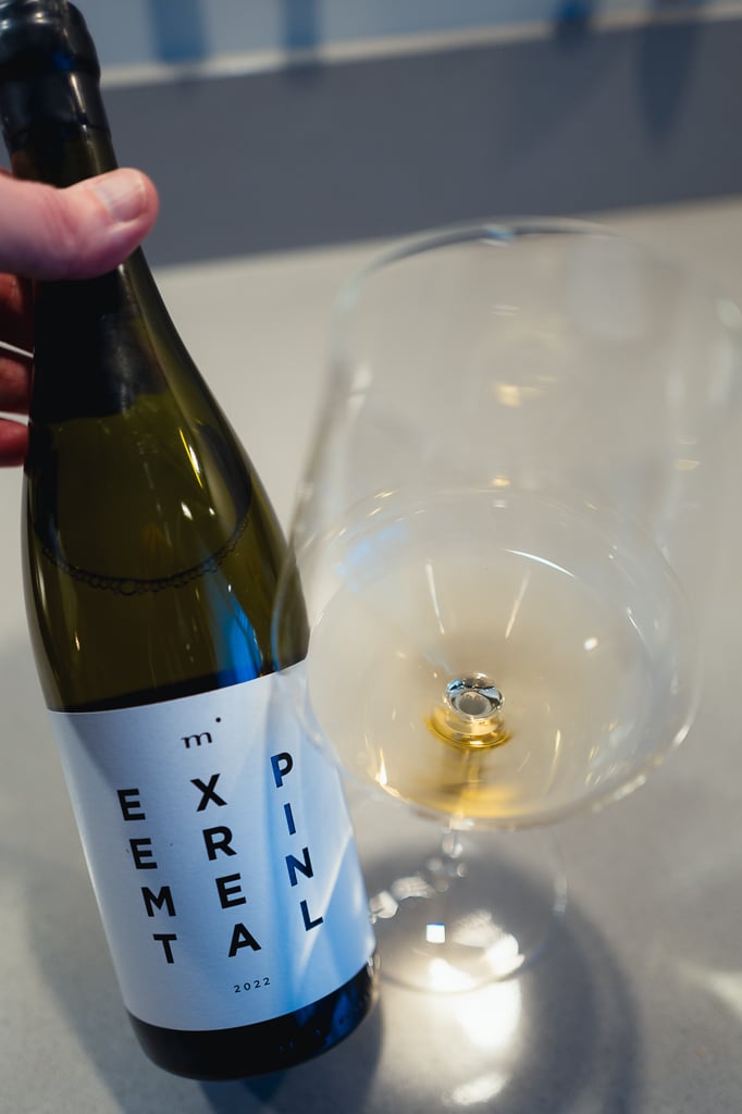 Minimalist Wines Experimental white bottle held beside a glass of pale white wine