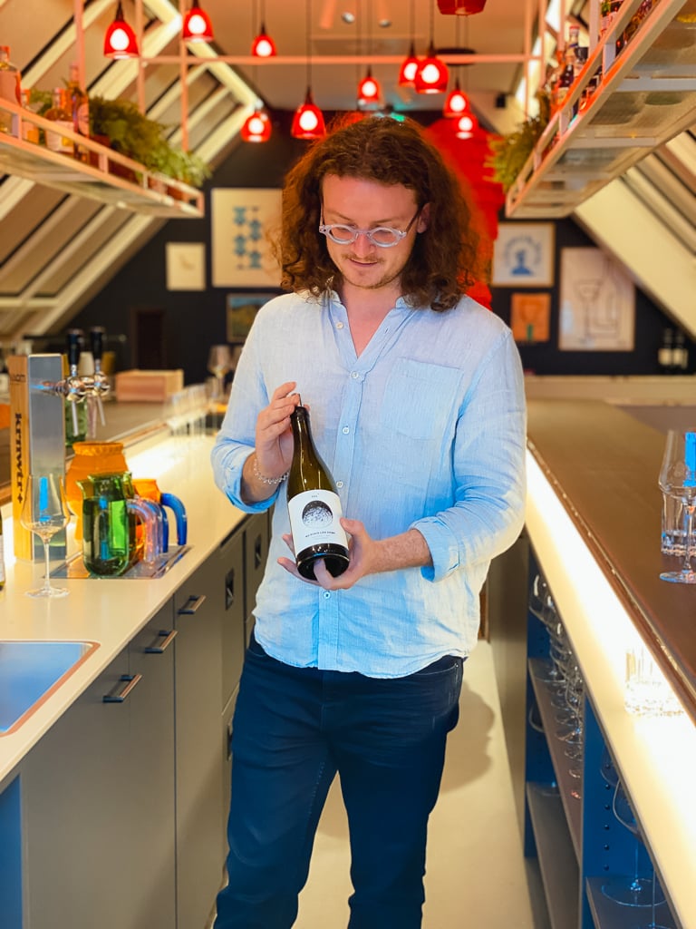 Winemaker Sam Lambson looking down at a wine bottle he is holding in a bar setting