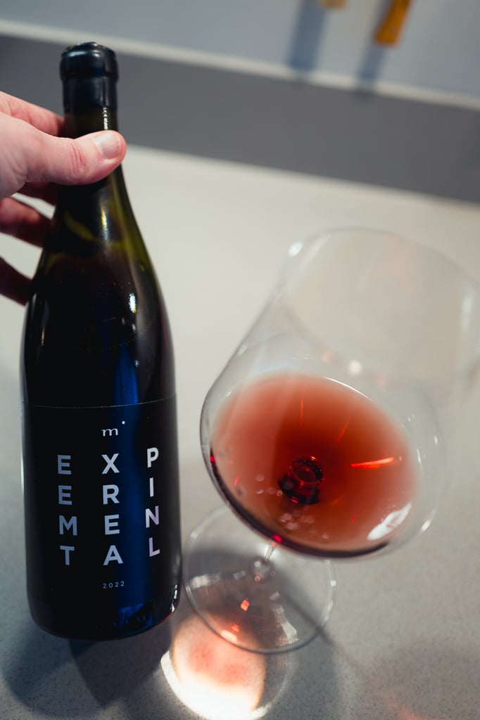 Minimalist Wines Experimental bottle held beside a glass of pale red wine
