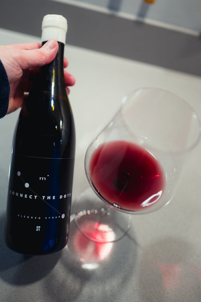 Minimalist Wines Connect the Dots bottle held beside a glass of red wine
