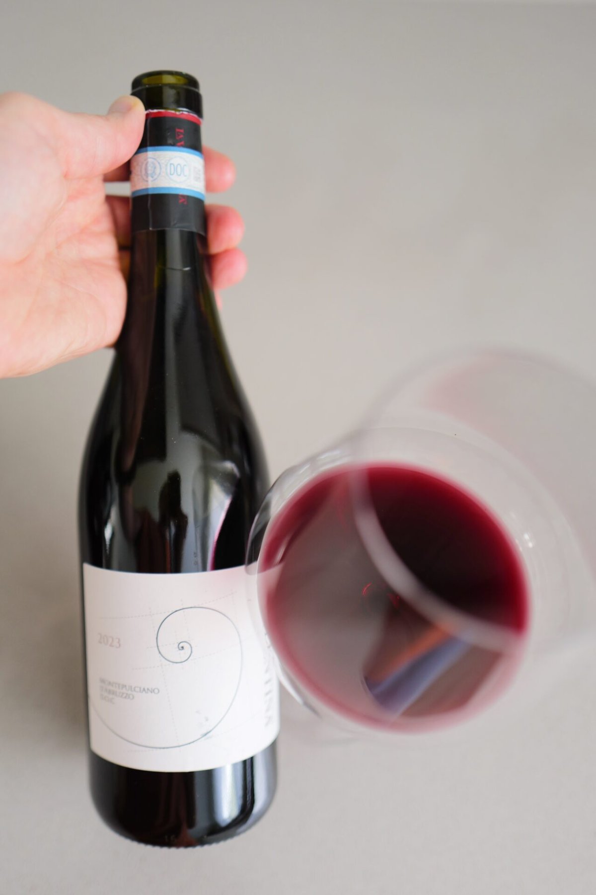 Hand holding a La Valentina Montepulciano bottle next to a glass of red wine