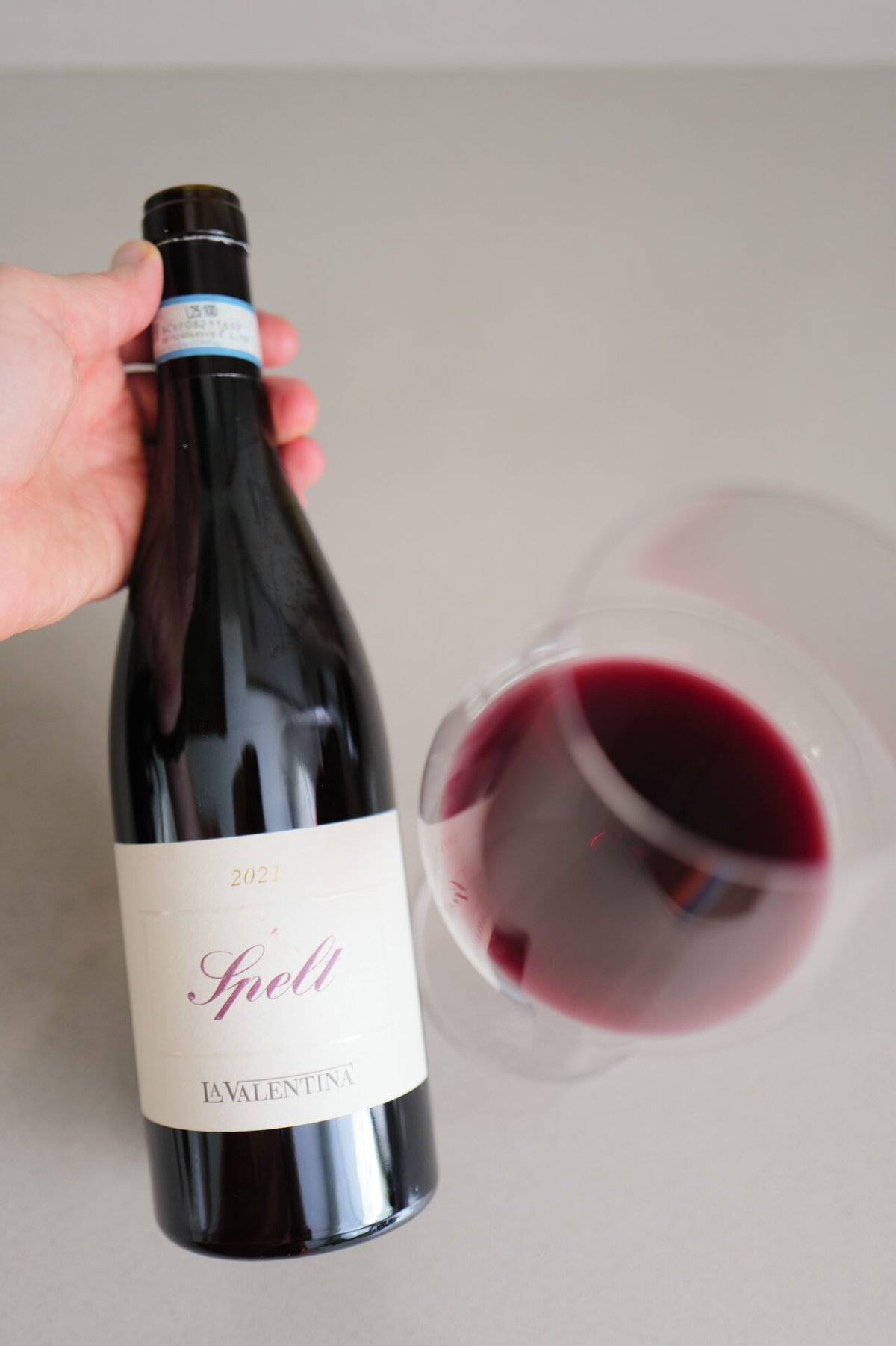 Hand holding a La Valentina Spelt Riserva bottle next to a glass of red wine