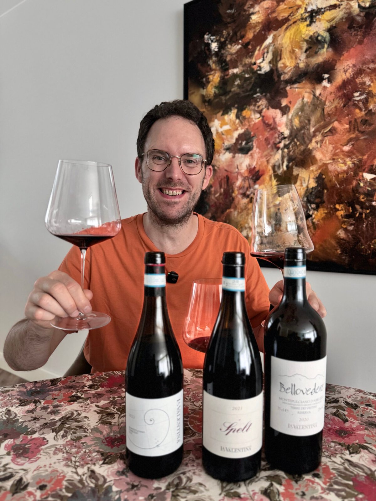 Smiling man raising a glass of red wine behind three La Valentina Montepulciano bottles