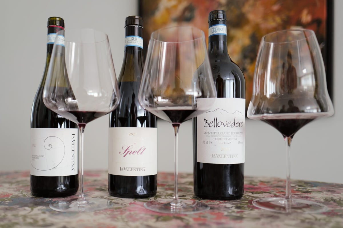 Three La Valentina Montepulciano bottles lined up with red wine glasses between them