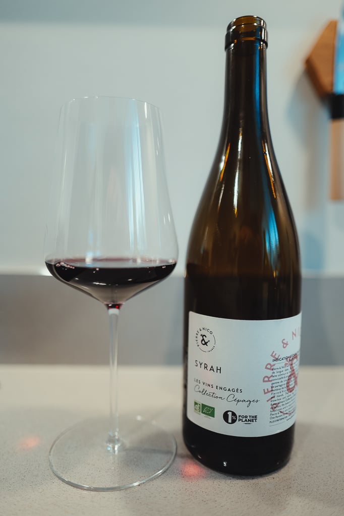 Pierre & Nico Syrah bottle beside a glass of red wine on a counter