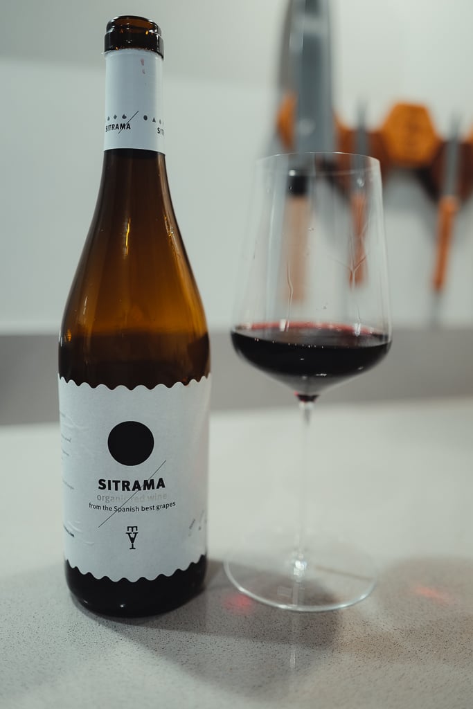 Sitrama organic bottle beside a glass of red wine on a counter