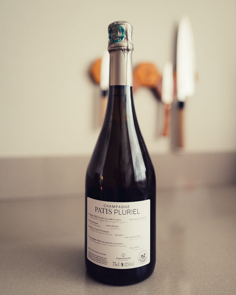 Back label of a Patis Pluriel champagne bottle with bilingual harvest text and capsule