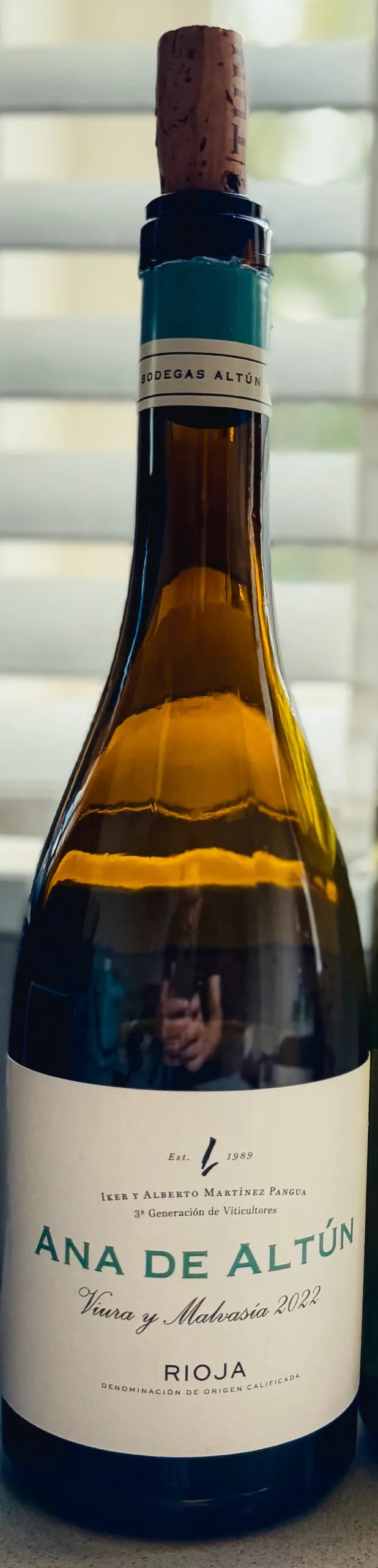 Ana de Altún Rioja white wine bottle with a cork resting on top, in front of a window