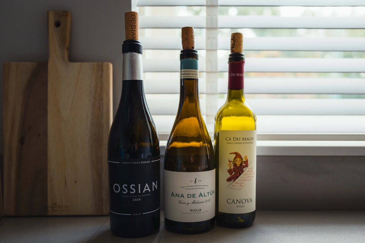 Three wine bottles, Ossian, Ana de Altún and Canova, lined up on a windowsill with blinds