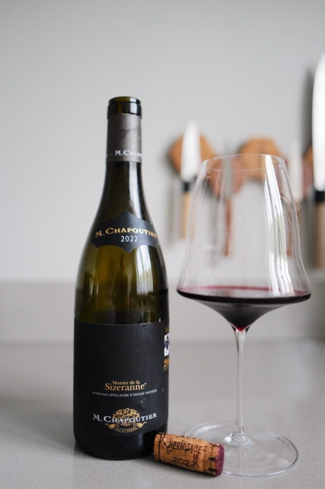 M. Chapoutier Sizeranne Hermitage bottle beside a glass of red wine and a cork on a counter