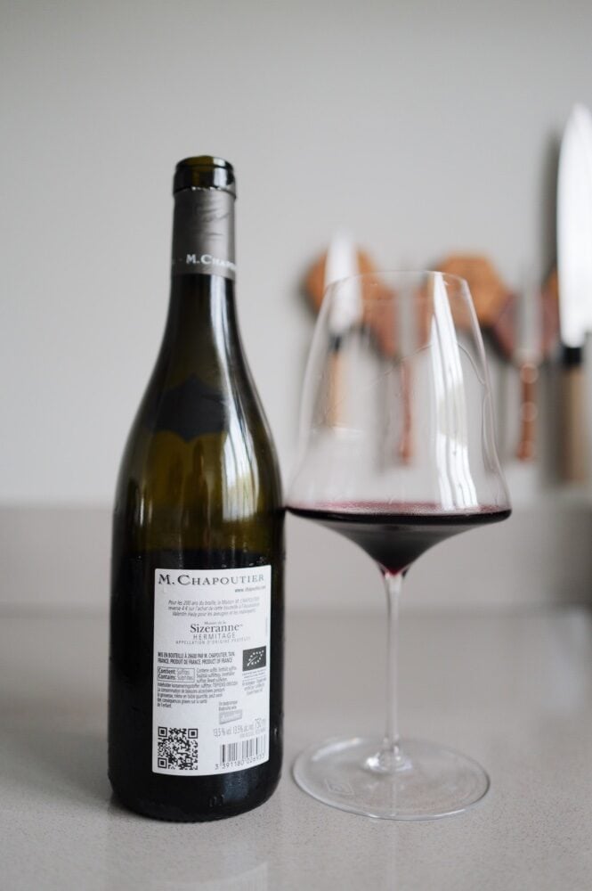 Back label of the M. Chapoutier Sizeranne Hermitage bottle next to a glass of red wine