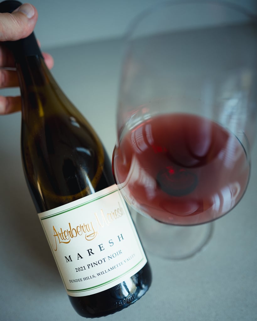 Hand holding the Arterberry Maresh Pinot Noir bottle over a tilted glass of pale red wine