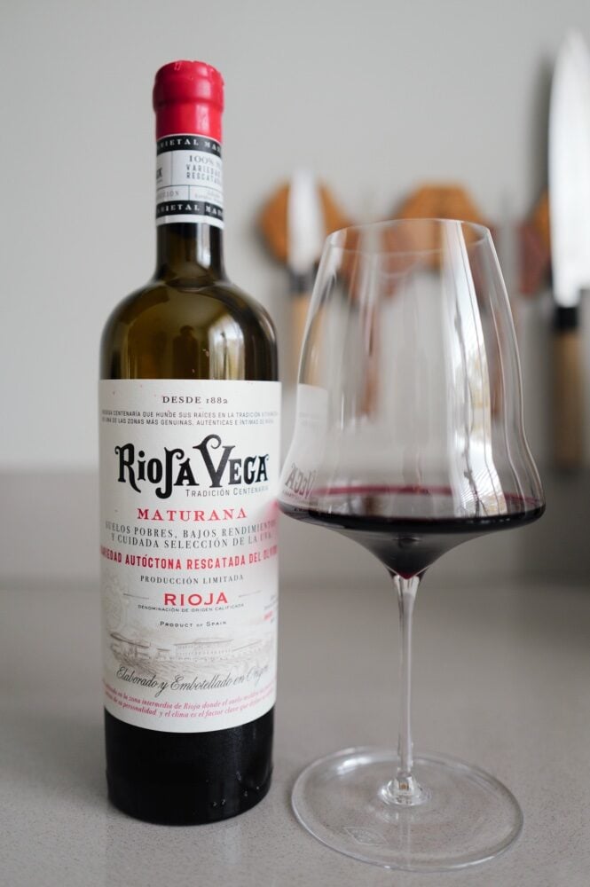 Rioja Vega Maturana red wine bottle with a red capsule beside a glass of dark red wine