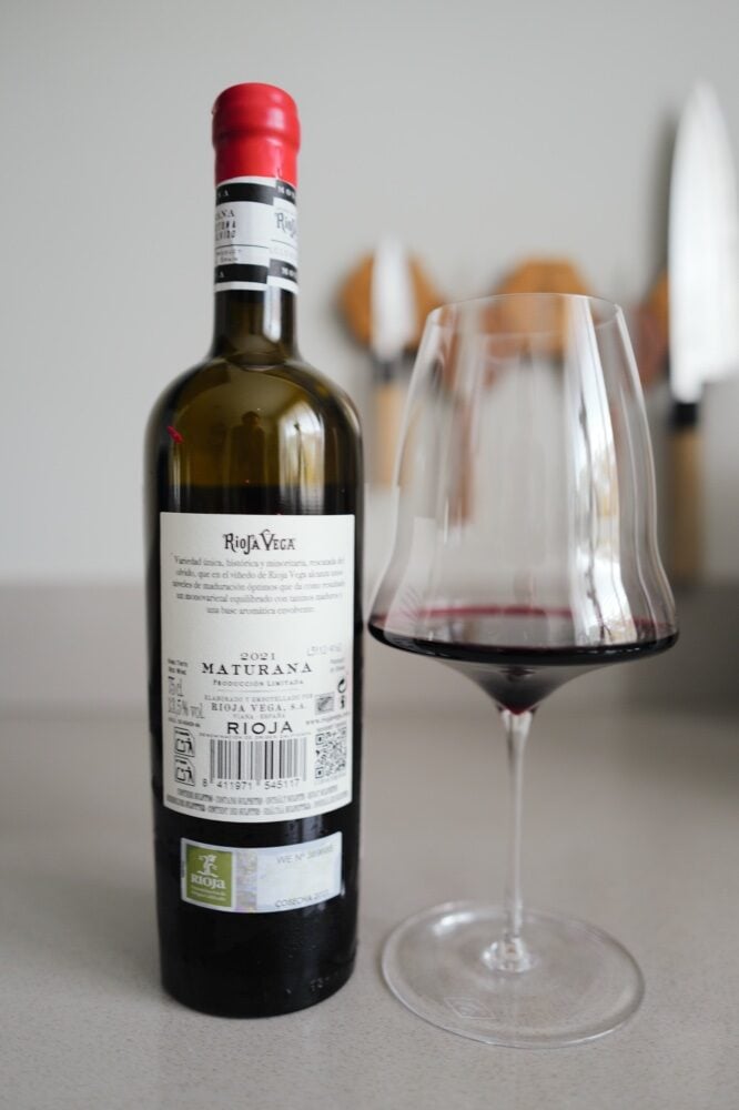 Back label of the Rioja Vega Maturana 2021 bottle next to a glass of dark red wine