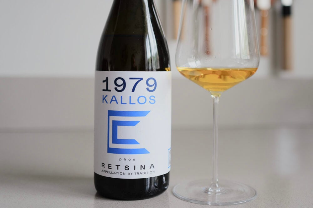 1979 Kallos Phos Retsina bottle beside a glass of deep golden wine on a counter