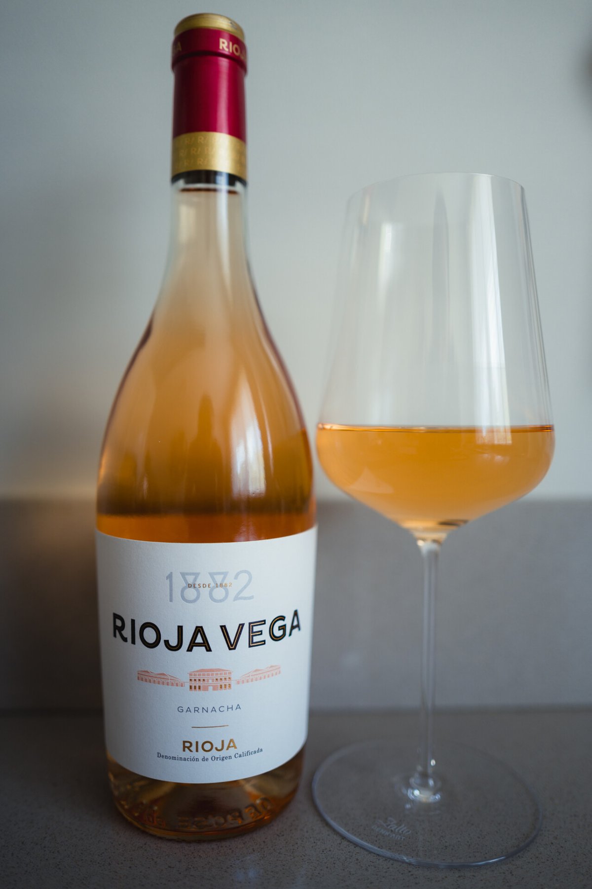 Rioja Vega Garnacha rosé bottle beside a glass of salmon-pink wine on a grey counter