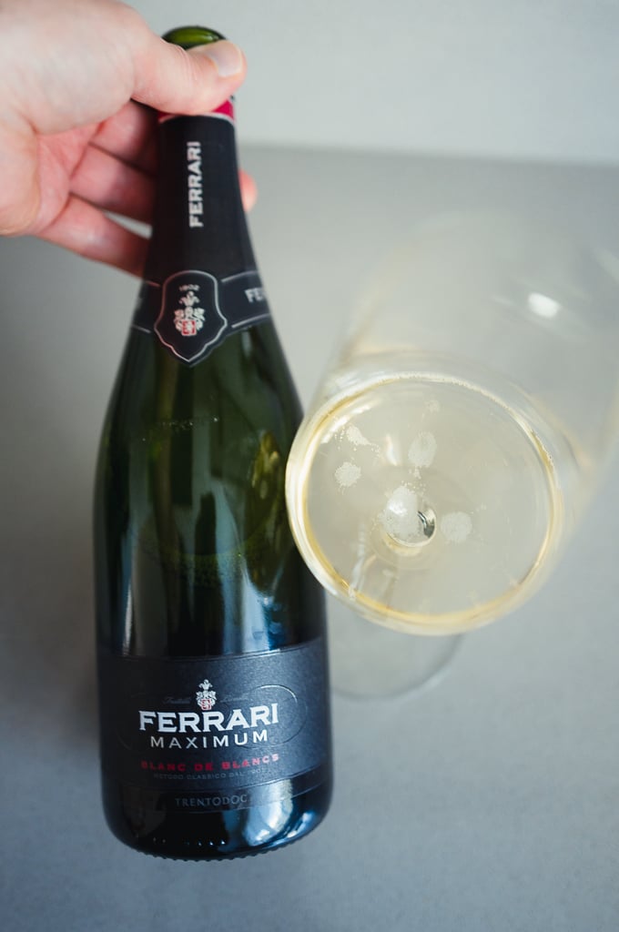 Hand holding a Ferrari Maximum Blanc de Blancs bottle beside a glass of sparkling wine