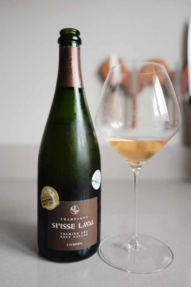 Suisse Laval Premier Cru Brut Nature champagne bottle beside a glass of golden sparkling wine