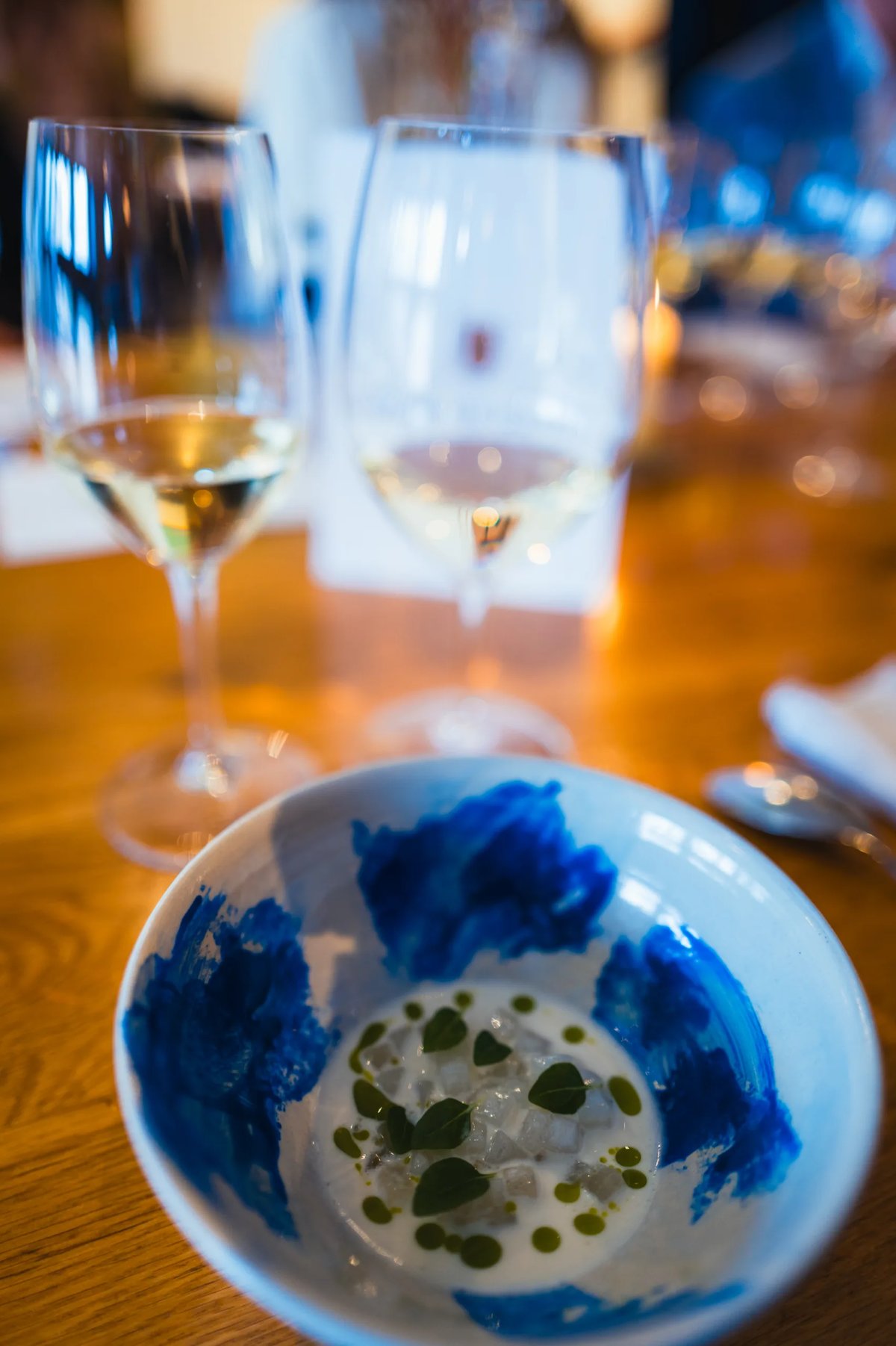 Blue-painted ceramic bowl holding a delicate dish, with two glasses of white wine behind it